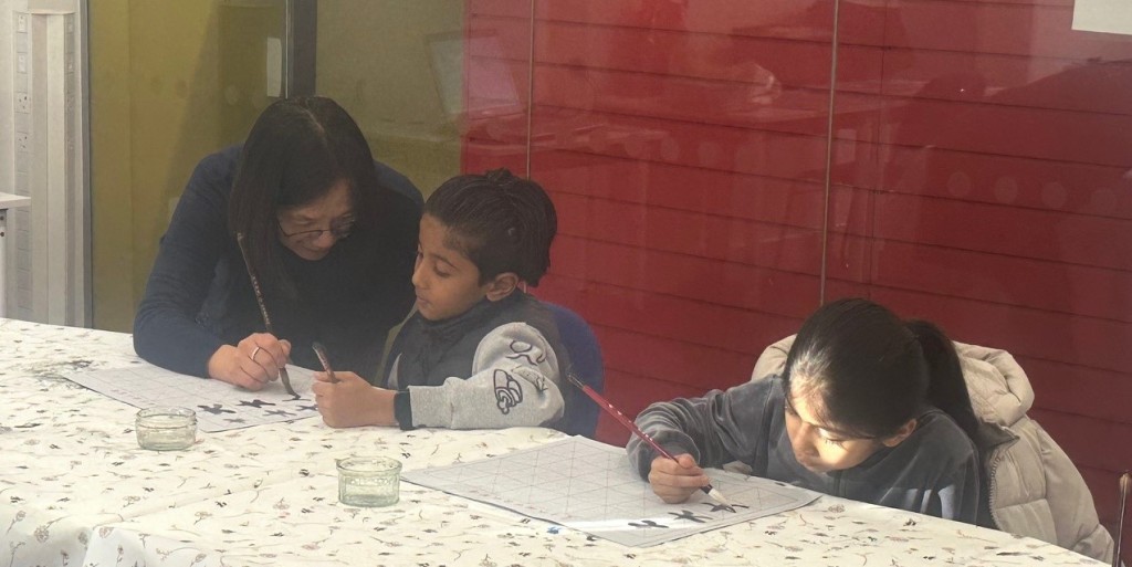 Photo of Anna helping the children with their brush strokes during the Chinese Calligraphy Workshop