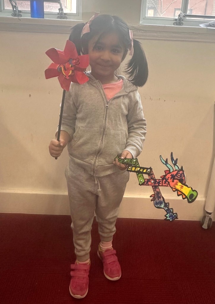 Photo of a child holding the wooden puppet and windmill she made during the craft session