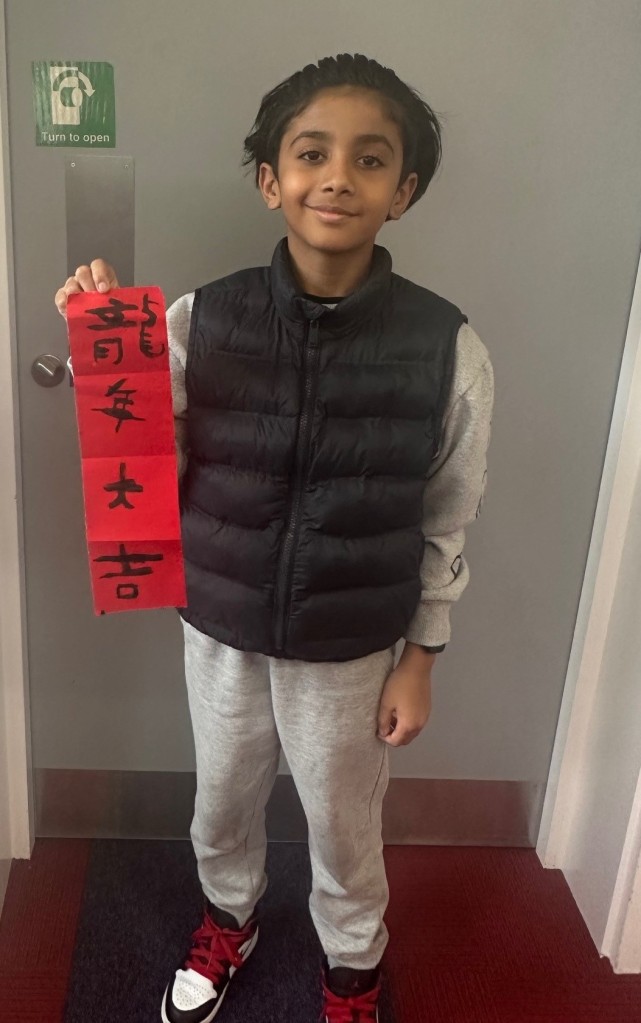 Photo of a child holding the red scroll showcasing his Chinese calligraphy