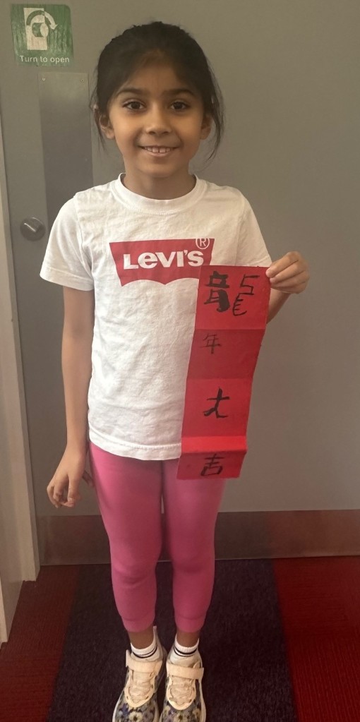 Photo of a child holding the red scroll showcasing her Chinese calligraphy